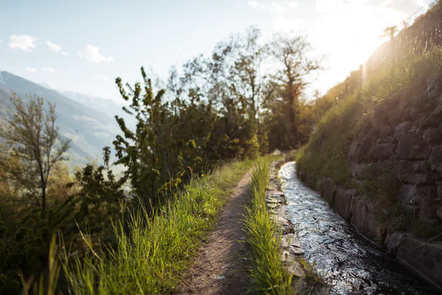 A canal trail leading through a green, mountainous landscape 